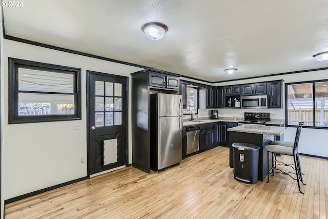 kitchen featuring a breakfast bar area, stainless steel appliances, ornamental molding, light hardwood / wood-style floors, and a kitchen island