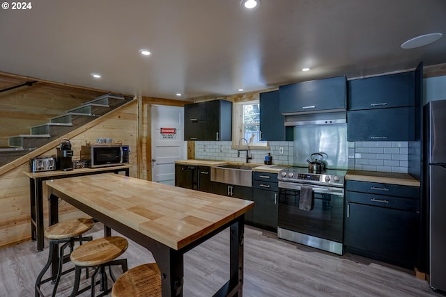 kitchen featuring wood walls, sink, appliances with stainless steel finishes, butcher block countertops, and light hardwood / wood-style floors