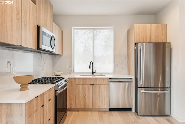 kitchen with light brown cabinets, sink, light wood-type flooring, appliances with stainless steel finishes, and tasteful backsplash