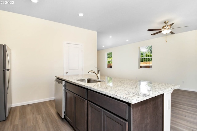 kitchen with a kitchen island with sink, sink, appliances with stainless steel finishes, light stone counters, and wood-type flooring