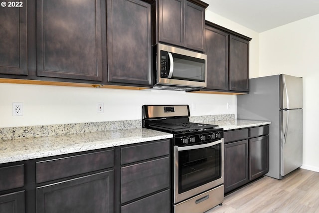 kitchen featuring dark brown cabinetry, light stone counters, stainless steel appliances, and light wood-type flooring