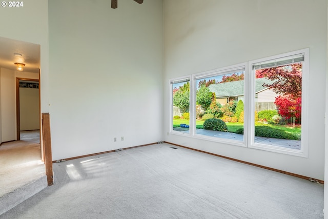 empty room with carpet flooring, a high ceiling, and ceiling fan