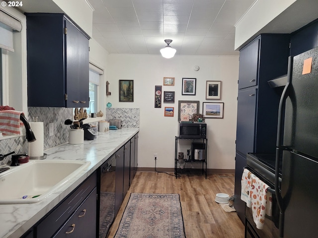 kitchen with light wood-type flooring, backsplash, light stone counters, sink, and black appliances