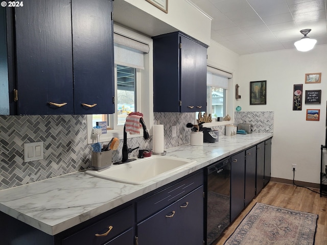 kitchen with sink, black dishwasher, light stone counters, light hardwood / wood-style flooring, and decorative backsplash