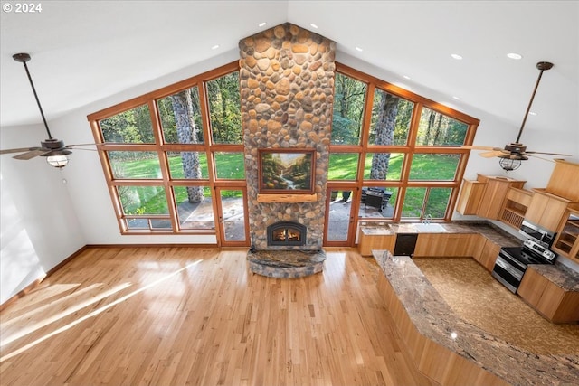 unfurnished living room with ceiling fan, high vaulted ceiling, a stone fireplace, and light hardwood / wood-style floors