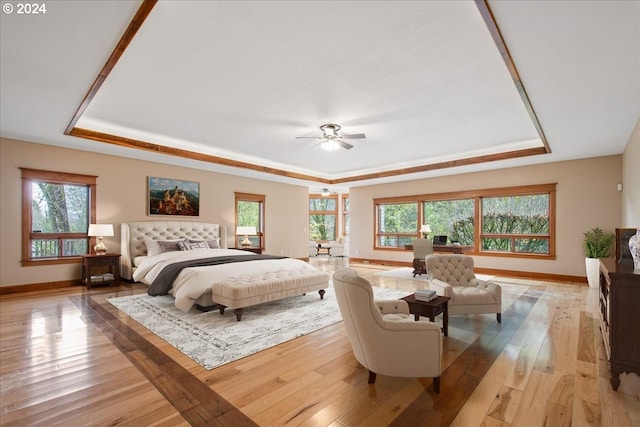 bedroom featuring ceiling fan, a tray ceiling, and light hardwood / wood-style flooring