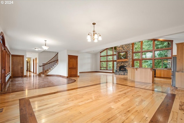 unfurnished living room featuring a notable chandelier, a fireplace, light hardwood / wood-style floors, and a healthy amount of sunlight