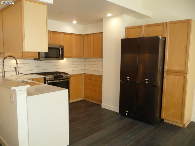 kitchen featuring stainless steel appliances, dark hardwood / wood-style flooring, backsplash, kitchen peninsula, and light brown cabinetry