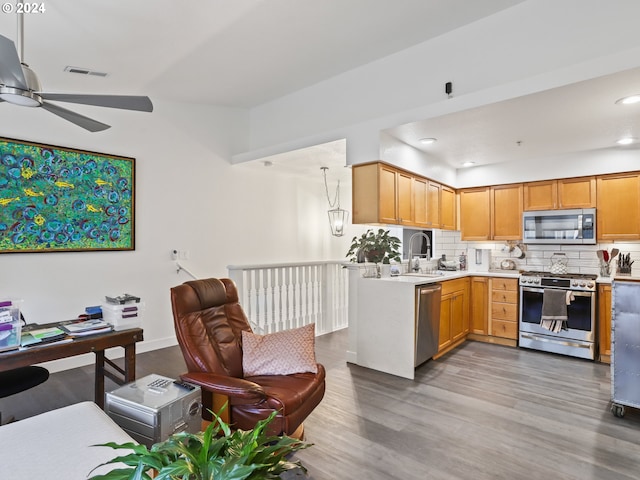 kitchen with backsplash, hanging light fixtures, kitchen peninsula, appliances with stainless steel finishes, and wood-type flooring