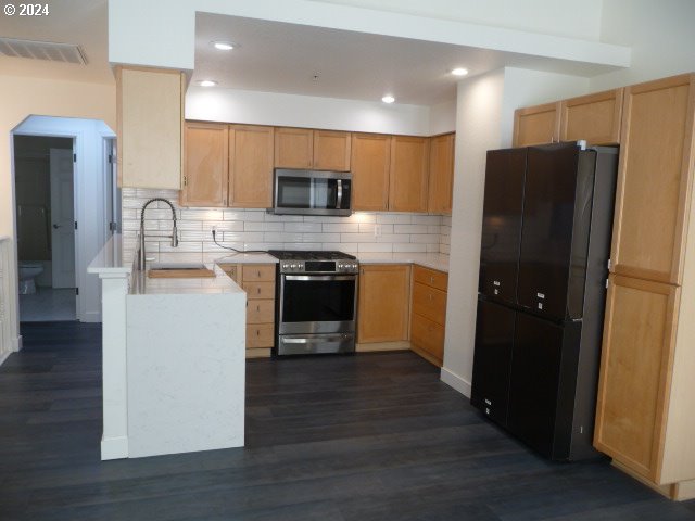 kitchen featuring decorative backsplash, light brown cabinetry, stainless steel appliances, dark wood-type flooring, and sink