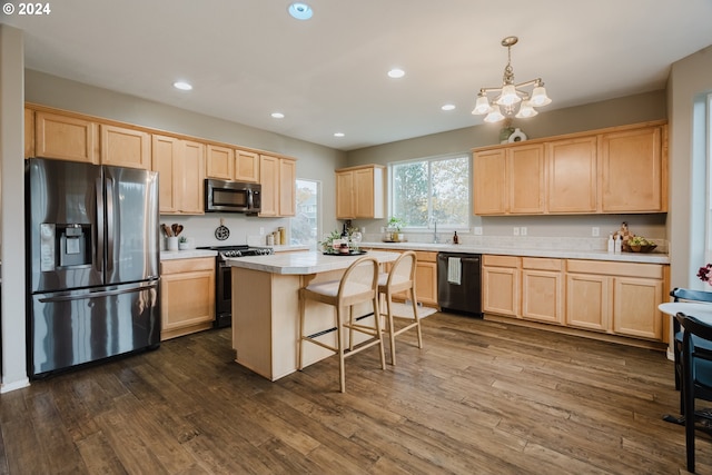 kitchen with light brown cabinets, dark hardwood / wood-style flooring, hanging light fixtures, and appliances with stainless steel finishes