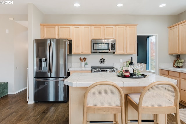 kitchen featuring dark hardwood / wood-style floors, tile countertops, light brown cabinetry, a breakfast bar, and appliances with stainless steel finishes