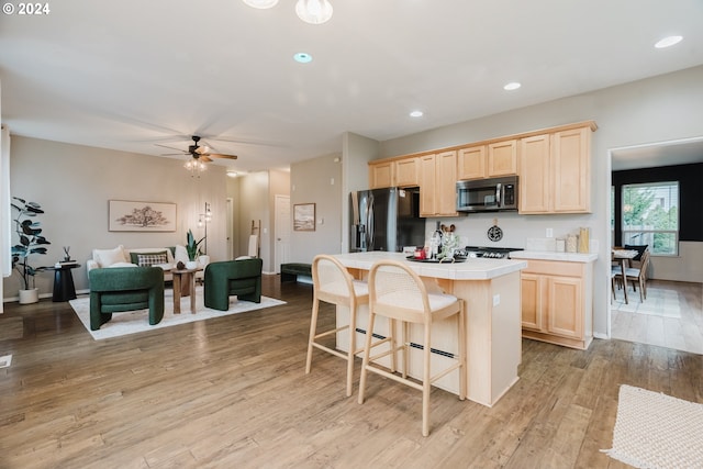 kitchen featuring ceiling fan, appliances with stainless steel finishes, tile counters, light hardwood / wood-style floors, and a kitchen bar