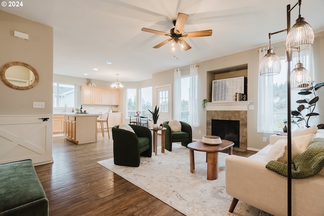 living room featuring a tile fireplace, ceiling fan with notable chandelier, and light wood-type flooring