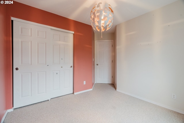 unfurnished bedroom featuring light carpet, a closet, and a notable chandelier