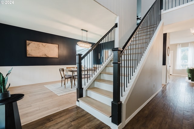 stairway with wood-type flooring and an inviting chandelier