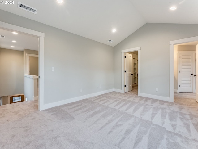 unfurnished bedroom with a walk in closet, light carpet, and vaulted ceiling