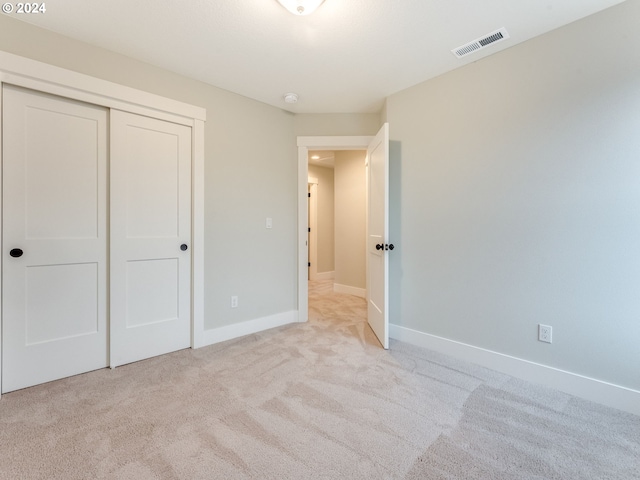 unfurnished bedroom with light colored carpet and a closet