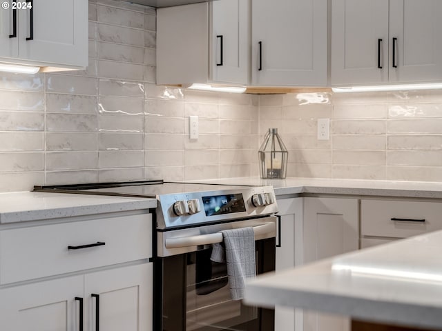 kitchen featuring white cabinets, light stone countertops, stainless steel range with electric stovetop, and backsplash