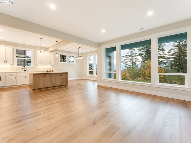 unfurnished living room featuring beamed ceiling, sink, light hardwood / wood-style flooring, and a notable chandelier