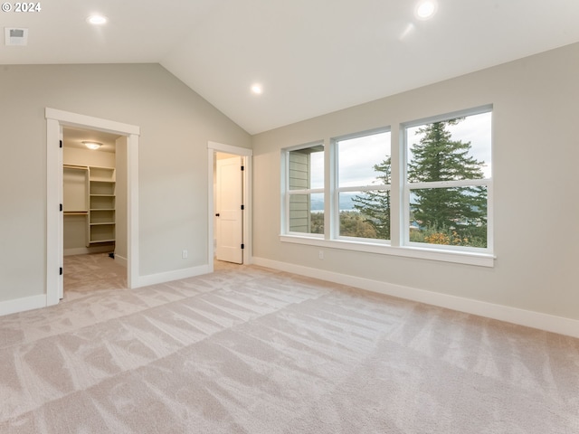 unfurnished bedroom featuring lofted ceiling, light carpet, a closet, and a walk in closet