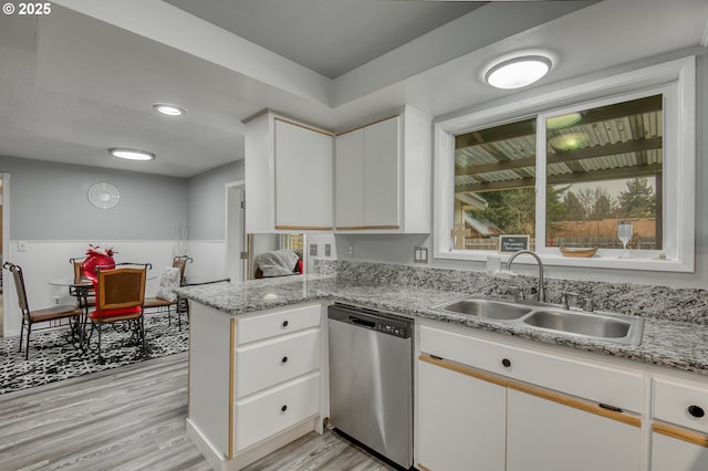 kitchen with a peninsula, stainless steel dishwasher, light wood-style floors, white cabinets, and a sink