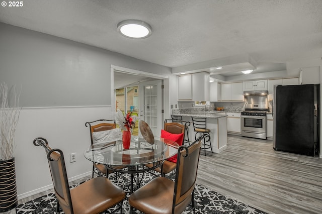 dining room featuring wainscoting, light wood-type flooring, and a textured ceiling