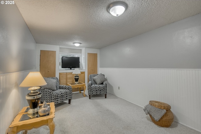 living area featuring carpet, wainscoting, and a textured ceiling