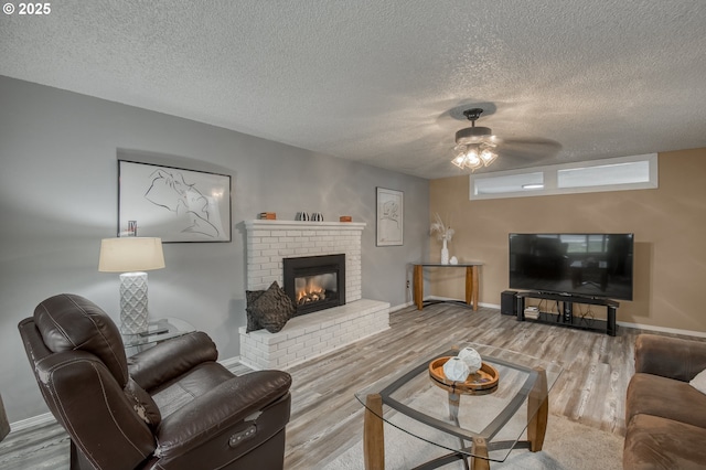 living room featuring wood-type flooring, a brick fireplace, a textured ceiling, and ceiling fan