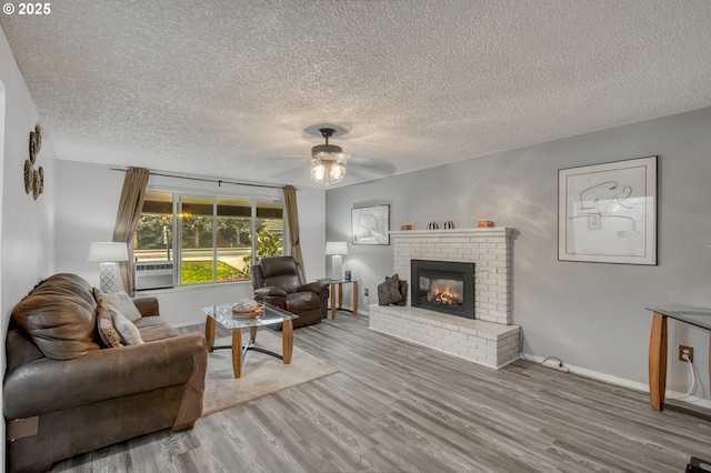 living room featuring a ceiling fan, wood finished floors, a fireplace, and a textured ceiling