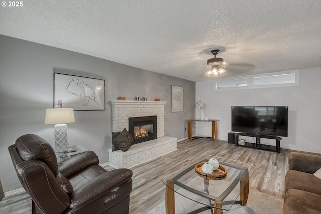 living room featuring a ceiling fan, a textured ceiling, wood finished floors, a fireplace, and baseboards