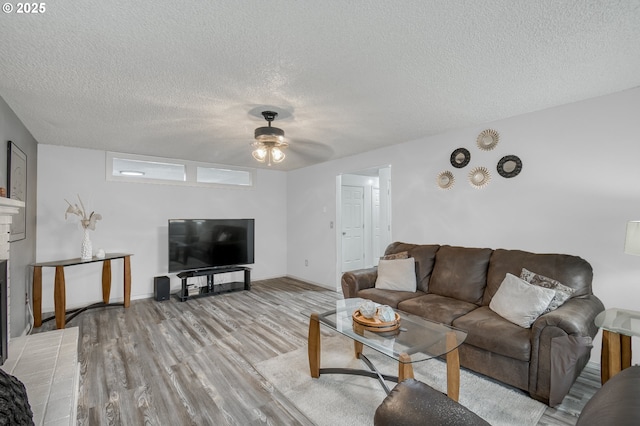 living area with a textured ceiling, a brick fireplace, wood finished floors, and ceiling fan