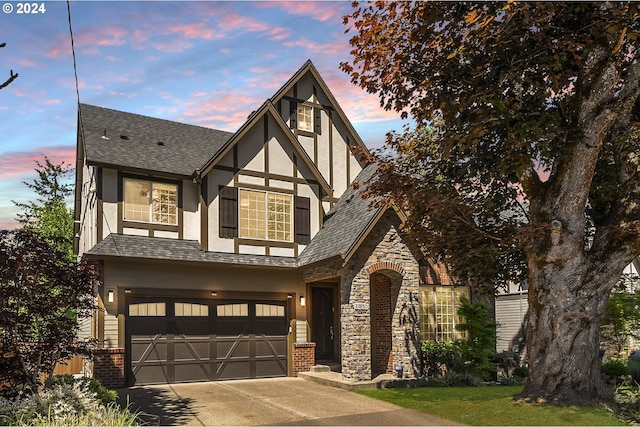 english style home featuring stone siding, brick siding, concrete driveway, and stucco siding