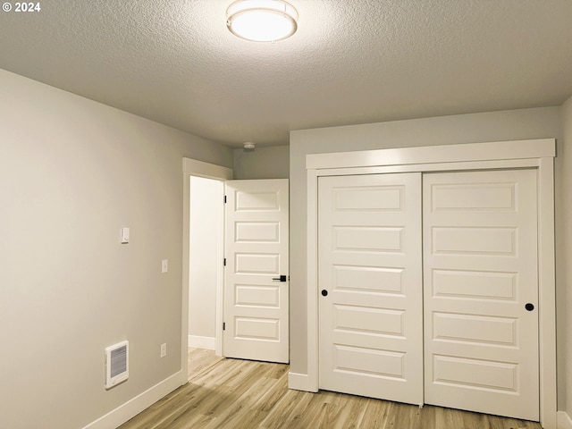 unfurnished bedroom featuring a textured ceiling, light wood-type flooring, and a closet