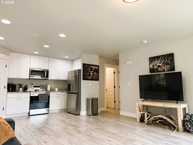 kitchen with light stone countertops, appliances with stainless steel finishes, white cabinets, and light hardwood / wood-style floors