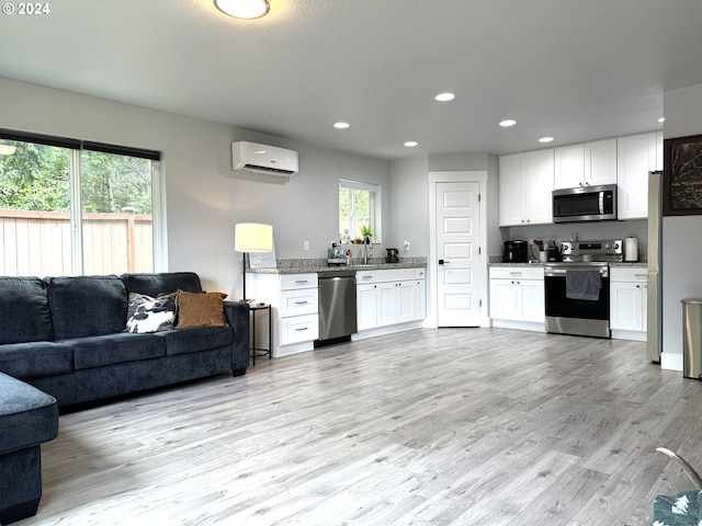 kitchen featuring stainless steel appliances, an AC wall unit, white cabinets, and light wood-type flooring