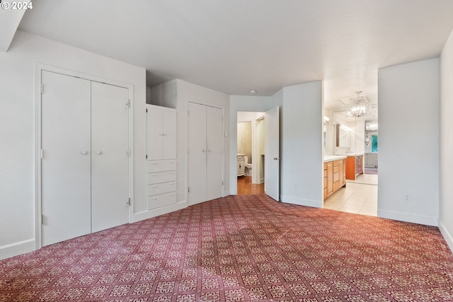 unfurnished bedroom with an inviting chandelier, light carpet, connected bathroom, and two closets