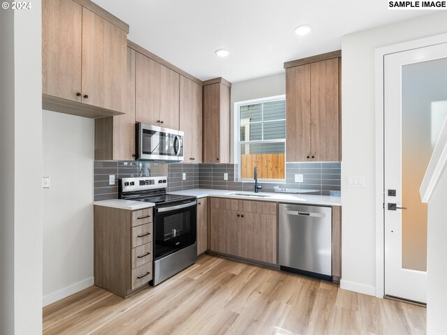 kitchen with light hardwood / wood-style floors, appliances with stainless steel finishes, tasteful backsplash, and sink