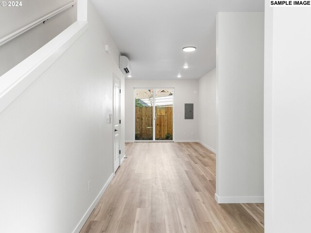 corridor with electric panel, light wood-type flooring, and a wall mounted air conditioner