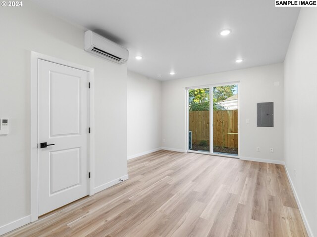 spare room featuring electric panel, light hardwood / wood-style flooring, and a wall unit AC