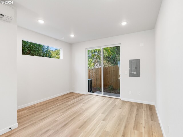 empty room featuring electric panel, light wood-type flooring, and a wall mounted AC