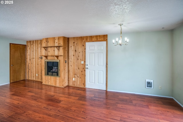 unfurnished living room featuring a textured ceiling, an inviting chandelier, dark wood-type flooring, and wood walls