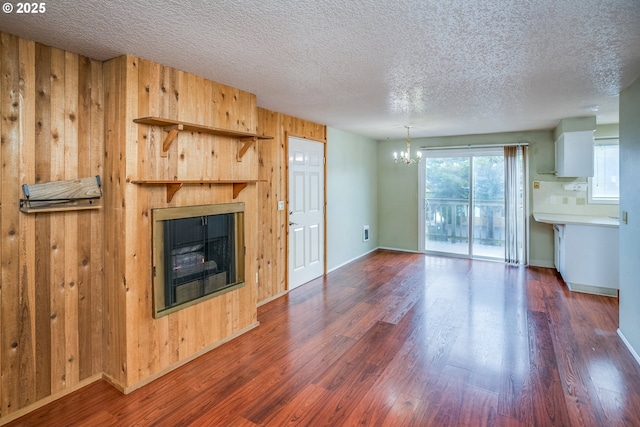 unfurnished living room with a textured ceiling, dark wood-type flooring, wooden walls, and a notable chandelier