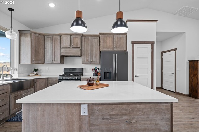 kitchen featuring light hardwood / wood-style floors, lofted ceiling, stainless steel refrigerator with ice dispenser, range with gas stovetop, and a kitchen island