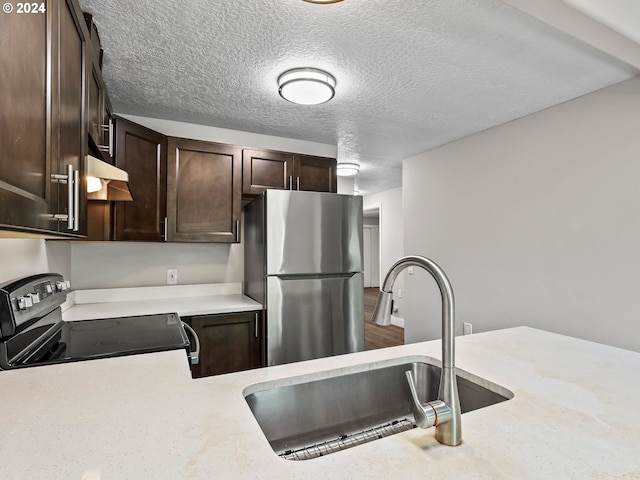 kitchen featuring sink, a textured ceiling, dark brown cabinetry, stainless steel refrigerator, and range with electric stovetop