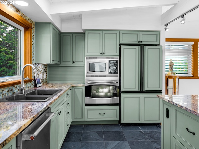 kitchen with sink, vaulted ceiling, green cabinetry, appliances with stainless steel finishes, and light stone counters