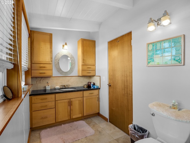 bathroom featuring backsplash, vanity, beamed ceiling, tile patterned flooring, and toilet