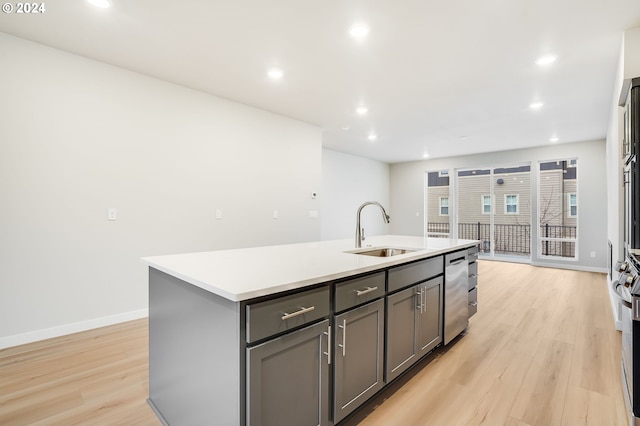 kitchen with a sink, a kitchen island with sink, light countertops, light wood-style floors, and stainless steel dishwasher