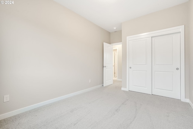 unfurnished bedroom with a closet, light carpet, and baseboards