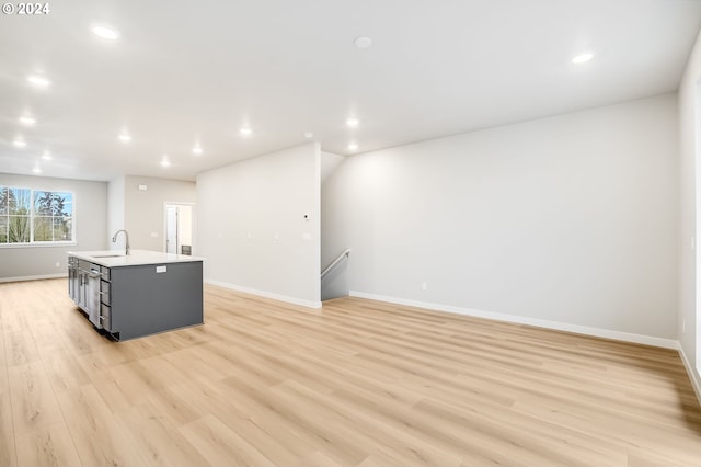 kitchen with an island with sink, light wood-style flooring, light countertops, a sink, and recessed lighting